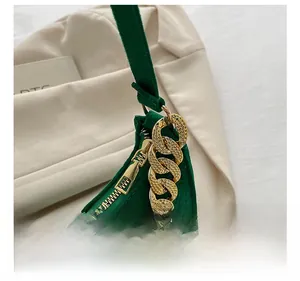 Detail shot of a dark green textured leather handbag with thick gold zipper and metal chain