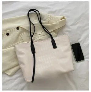 Detail view of cream tote bag featuring embossed diamond texture and black leather straps