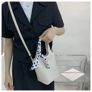 Detailed view of white bucket bag with decorative polka dot silk scarf and thin strap