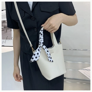 Close-up of white minimalist bucket bag featuring a polka dot silk scarf and thin strap