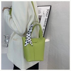Detail of green bucket bag with polka dot scarf handle and sleek leather finish
