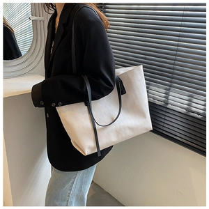 Close-up of a beige quilted tote bag with black strap worn by a model in a black suit