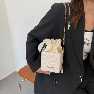 Minimalist beige quilted bucket bag with chain strap shown on a cross-body model