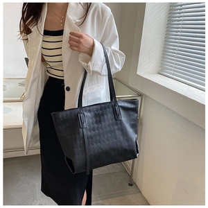 Close-up of a model wearing a black woven leather tote bag with a white formal blazer