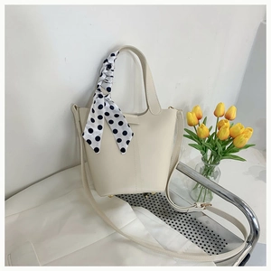 Detail of cream bucket bag with silk scarf handle and golden protective metal feet