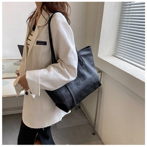 Close-up of a large black tote bag with quilted texture worn by a model in a suit