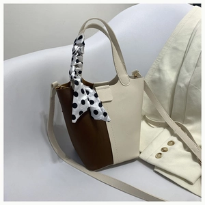 Close-up of a two-tone bucket bag with a polka dot silk scarf handle and thin strap