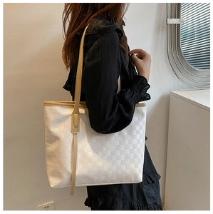 Detail of white checkered tote bag with brown straps worn by model against white wall