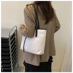 Detail of a large checkerboard tote bag with black straps carried by a model on shoulder