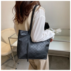 Detailed view of black checkered tote bag with tassel detail worn by a model