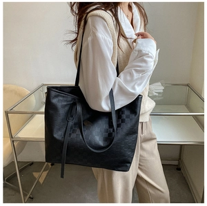 Detail of a large black tote bag with woven square texture worn by a model