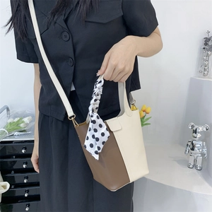 Brown and beige bucket bag with silk scarf handle displayed on a stylish pedestal