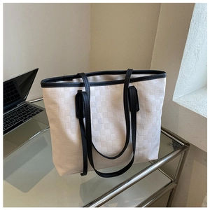 Detail of off-white checkered tote bag with black straps on a glass office desk