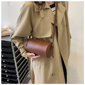 Brown cylindrical crossbody bag in synthetic leather shown on a model with a beige trench coat