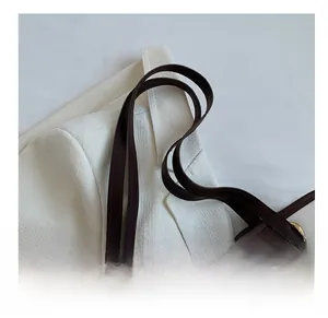 Dettaglio della tracolla in pelle marrone scuro con anelli dorati su una borsa bianca