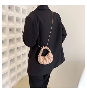 Detailed side view of beige pleated cloud bag with elegant gold chain strap on shoulder