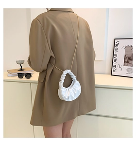 Detailed close-up of white ruched cloud bag with golden chain strap on a model