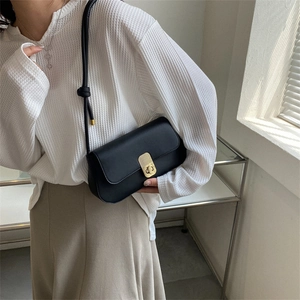 Minimalist black faux leather shoulder bag with golden metal lock worn by a model