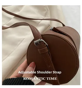 Detail of adjustable shoulder strap on dark brown cylindrical crossbody bag with silver buckle