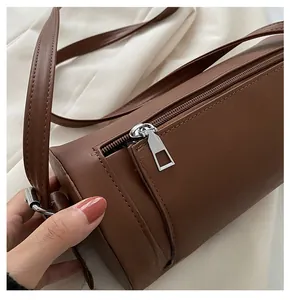 Detail of a smooth silver zipper and leather texture on a dark brown cylinder bag