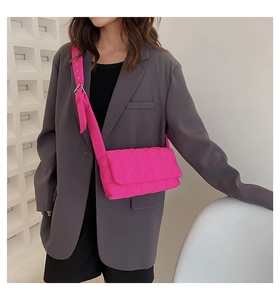 Detail of rose pink quilted crossbody bag with wide strap on a grey suit model outfit