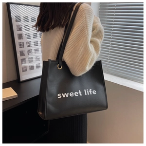 Dettaglio borsa shopper nera in pelle con testo e anelli in metallo dorato