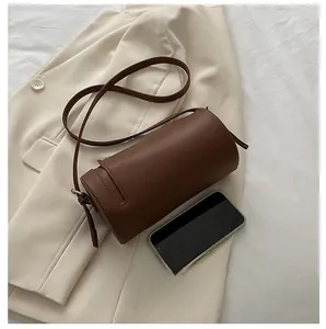 Brown leather cylinder shoulder bag shown next to a smartphone for size perspective