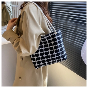 Close-up of black and white checkered tweed tote bag with woven rope handles on shoulder