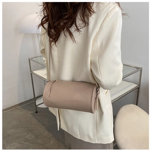 Detail of a minimalist khaki cylindrical crossbody bag worn by a model in a modern interior