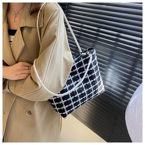 Shoulder view of a black and white checkered tweed tote bag with woven rope handles