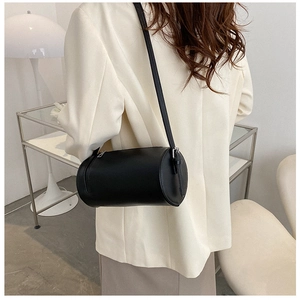 Side view of a black cylindrical leather crossbody bag paired with a white blazer