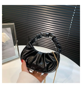 Detail of black pleated cloud bag with circular handle and elegant gold chain strap