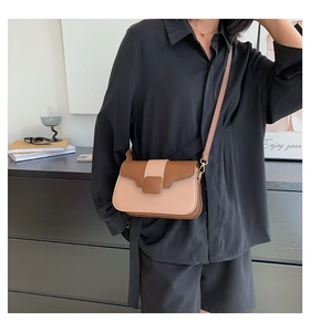 Detail of a two-tone crossbody bag in brown and beige worn by a model in a minimal setting