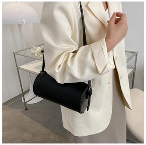 Chic black matte leather cylinder bag worn with a white blazer for a minimalist look