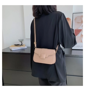 Beige crossbody bag with gold square buckle shown as part of a stylish fashion outfit
