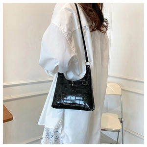 Detail of black croc-embossed underarm bag with glossy finish and metal hardware