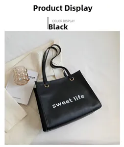 Dettaglio della borsa tote in pelle nera con scritta bianca e fibbie dorate in metallo
