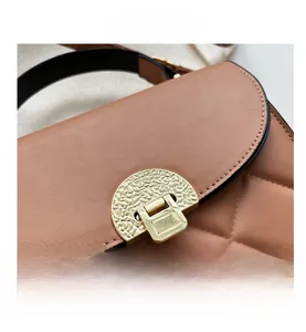 Close-up of caramel quilted crossbody bag with golden textured lock and black trim