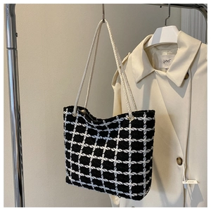 Detail of black and white plaid tweed tote bag with woven rope handles on a trench coat