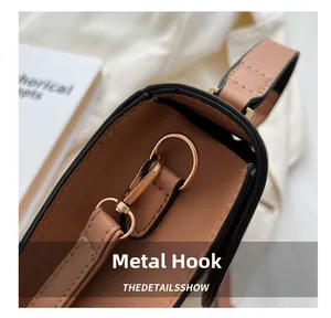 Close-up of high-gloss gold lobster clasp and stitching on brown leather handbag