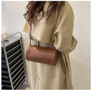 Detail view of a brown cylindrical leather crossbody bag paired with a khaki trench coat