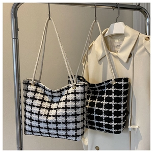 Detail of woven plaid tote bags with rope handles hanging on a rack against a trench coat