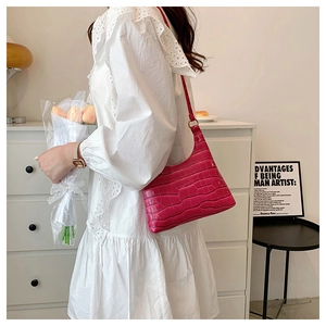 Detail of fuchsia crocodile pattern shoulder bag held by model in elegant home setting