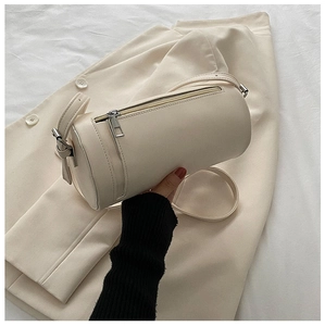 Detail of cream cylindrical crossbody bag with top zipper on neutral background