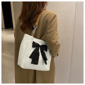 Détail du sac à bandoulière blanc plissé avec nœud noir et bandoulière en cuir brun