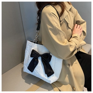 Détail du sac plissé blanc avec nœud noir et bandoulière en chaîne argentée sur l'épaule