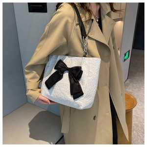 Détail du sac cabas plissé blanc avec un grand nœud noir et une bandoulière à chaîne