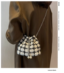 Detail of tweed bucket bag with pearl accents and chain strap on a brown coat