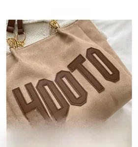 Detail of HOOTO embroidery on a light brown suede tote with gold chain strap design