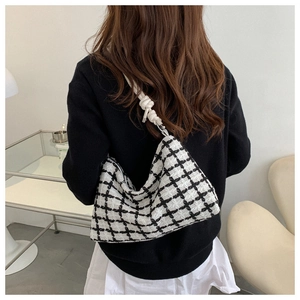 Detail of checkered tote bag with woven rope handle worn by a model in a modern room